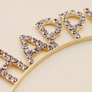 Dettaglio macro di strass scintillanti con scritta HAPPY su cerchietto dorato per feste
