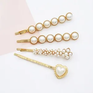 Détail de quatre barrettes dorées avec perles blanches artificielles de formes géométriques