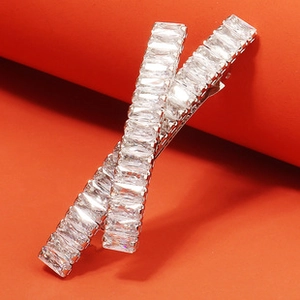 Macro shot of silver X-shaped hair clip with baguette-cut rhinestones on orange background