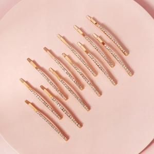 Nahaufnahme von 12 goldenen Strass-Haarklammern auf einer rosa Keramikplatte