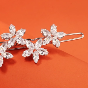 Vue macro d'une barrette argentée avec trois fleurs en zircon sur une surface orange