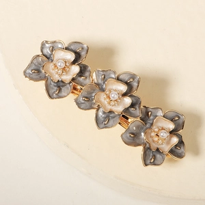 Détail d'une barrette florale avec pétales gris, perles blanches et cadre en métal doré