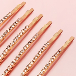 Detailaufnahme von fünf goldenen Metall-Haarspangen mit Strass auf rosa Hintergrund