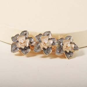 Détail de barrette dorée élégante avec fleurs en émail et perles centrales blanches