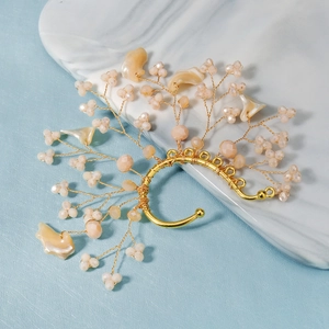 Detailed shot of handmade golden flower ear cuff with pearls and beads on marble tray