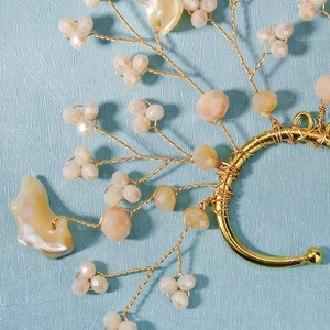 Macro shot of handmade gold wire bridal ear cuff with peach beads and shell details