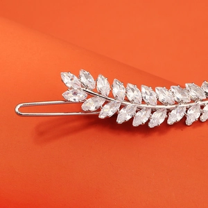 Close-up of silver hair clip with marquise-cut zircon leaf patterns on orange background
