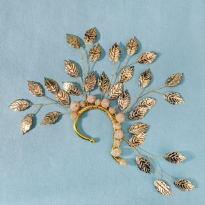 Close-up of golden leaf bridal ear cuff with pink beads on a light blue background