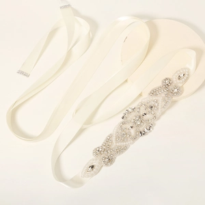 Macro detail of hand-sewn pearls and crystals on ivory satin wedding belt with floral motifs