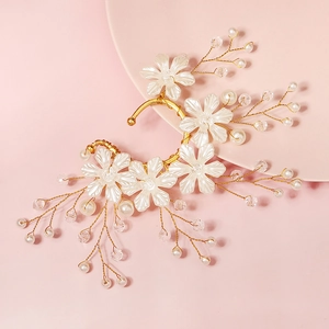 Detail of bridal ear cuff with white flowers and pearls on a soft pink background