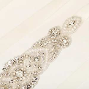 Close-up of handmade bridal belt with pearls and rhinestones on off-white satin ribbon