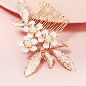 Detail of bridal hair comb featuring white enamel flowers and pearls on golden metal