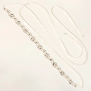 Close-up of bridal sash with wavy rhinestone and pearl embellishments on white satin