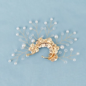 Detail of handcrafted gold floral ear cuff with pearls and crystal beads on a blue surface