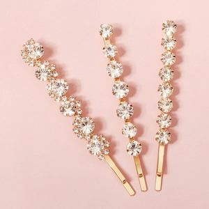 Golden S-shaped and linear hair clips set with sparkling rhinestones on pink background