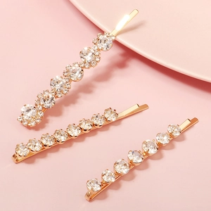 Three-piece gold metal hair clip set with sparkling rhinestones on pink background