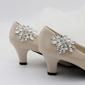 Close-up of beige patent pumps featuring a large sparkling rhinestone flower buckle decoration
