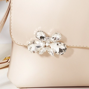 Close-up of a luxury beige leather bag featuring a large sparkling rhinestone butterfly buckle