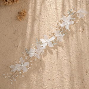 Elegant bridal hair vine with white fabric flowers and pearls on a textured background