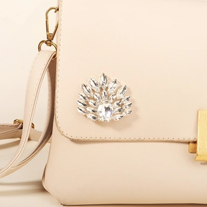 Macro shot of sparkling rhinestone feather shoe clip on a white leather clutch