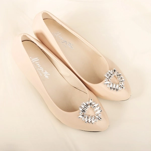 Macro shot of sparkling crystal shoe clip on pointed-toe nude patent leather flat shoes
