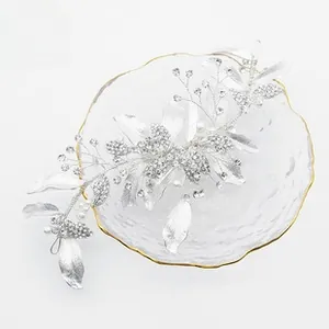 Detailed view of bridal hair piece with silver leaves, crystals, and pearls on glass tray