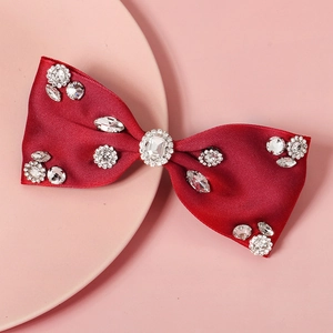 Detailed macro view of a red satin bow hair clip adorned with sparkling rhinestones