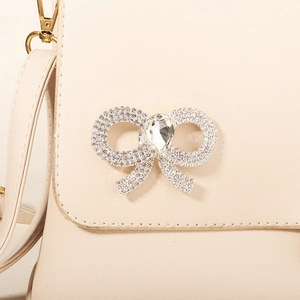 Detailed macro view of a beige PU leather bag with large rhinestone bowtie ornament