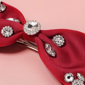 Detailed view of a red fabric bow hair clip featuring sparkling white rhinestones