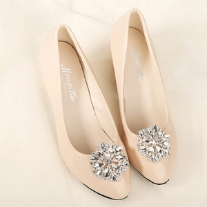 Detail shot of radial crystal flower buckle on elegant beige patent leather flat shoe