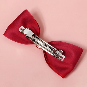 Elegant red fabric bow hair clip with silver metal spring fastener on pink background