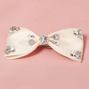 Detail of elegant beige bow hair clip featuring sparkling rhinestones and metal spring clip