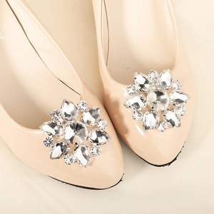 Close-up of sparkling rhinestone flower clips on elegant beige patent leather flat shoes