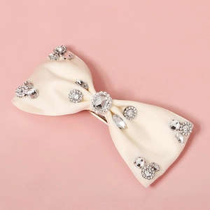 Close-up of elegant cream satin bow hair clip with sparkling rhinestones on pink background