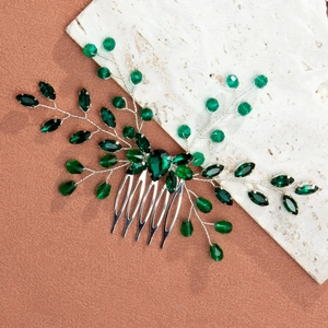 Macro shot of silver bridal hair comb with deep emerald crystals and leaf-shaped metal details
