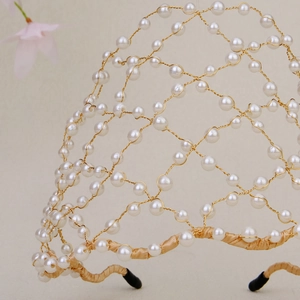 Close-up of golden wire mesh bridal headband with white pearls and satin wrapped base
