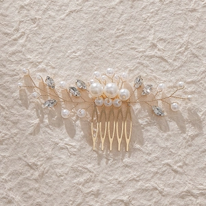 Elegant gold bridal hair comb with white pearls and rhinestones on a textured background