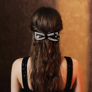 Detail of a black bridal bow hair clip with white pearls and gold embroidery on dark hair