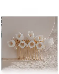 Détail d'un peigne à cheveux de mariée avec fleurs en argile blanche et perles sur fil doré