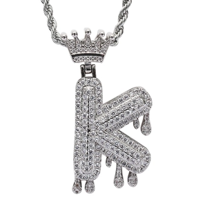 Macro detail of iced-out silver letter K pendant with crown and dripping effect