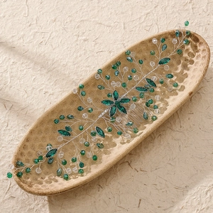 Detail of emerald crystal bridal hair comb with silver wire flowers on ceramic plate