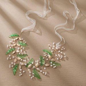 Bandeau de mariée doré avec feuilles vertes et perles sur fond texturé beige