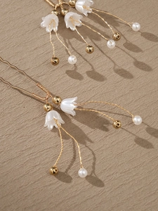 Detailed view of lily of the valley hair pin with white pearls and gold tassel on fabric