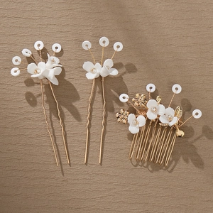 Detail of white ceramic flowers and golden wire on bridal hair comb and pins
