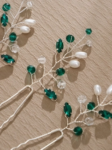 Macro detail of U-shaped hair pins with green gems, white pearls and silver wire weaving