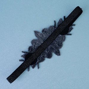 Détail d'un bandeau élastique noir orné d'une applique florale en dentelle grise perlée