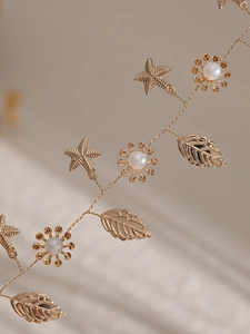 Detailaufnahme von goldenem Blatt- und Seestern-Brauthaarschmuck mit Perlen und Draht