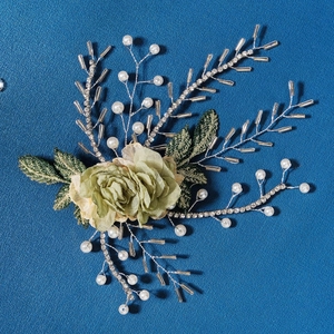 Handmade bridal hairpiece with green fabric flowers and white pearls on blue background