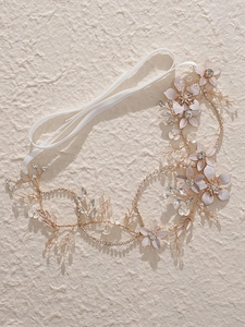Détail d'un bandeau de mariée artisanal avec fils dorés, fleurs roses et perles blanches