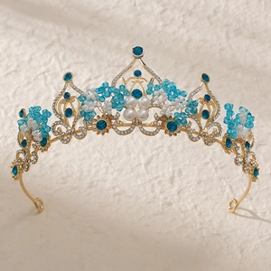 Baroque bridal crown with gold plating, blue rhinestones and white pearls on beige surface